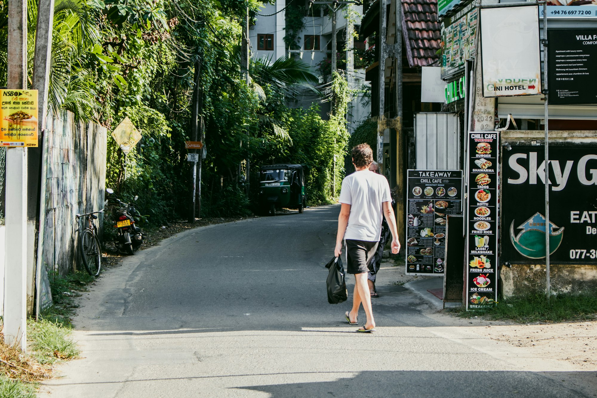 A quiet tropical town street with shopfronts and a passer-by