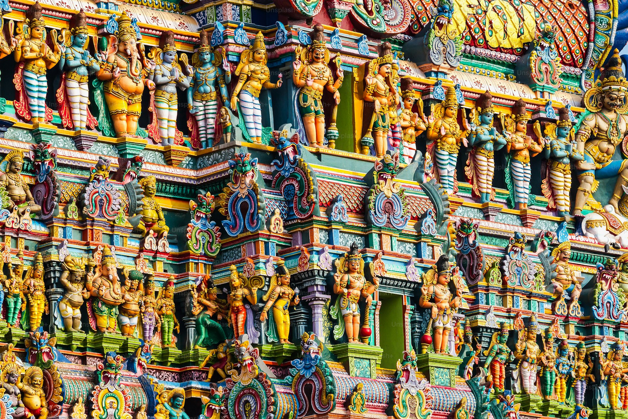 Brightly painted figures carved across the gopuram tower of a Hindu temple